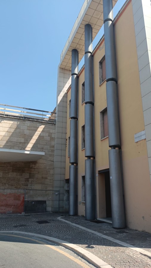 Modern building exterior featuring tall cylindrical metal columns and a flat roof, against a clear blue sky.