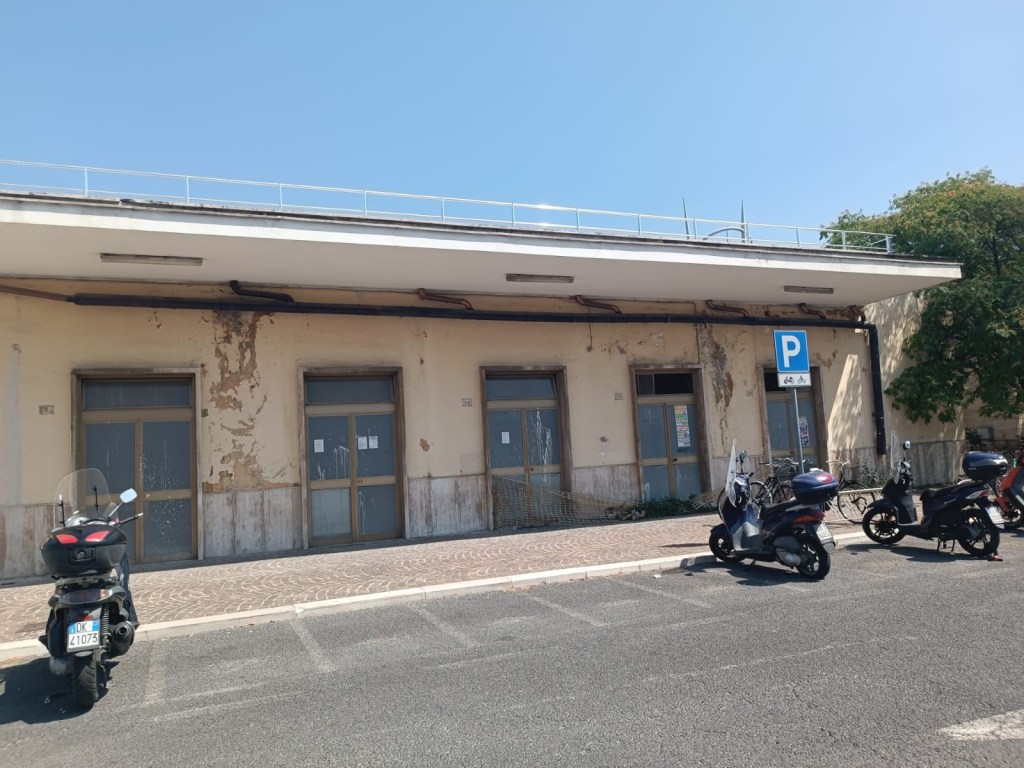 Exterior view of an old building with peeling paint and several parking spaces for scooters in front, under a clear blue sky.