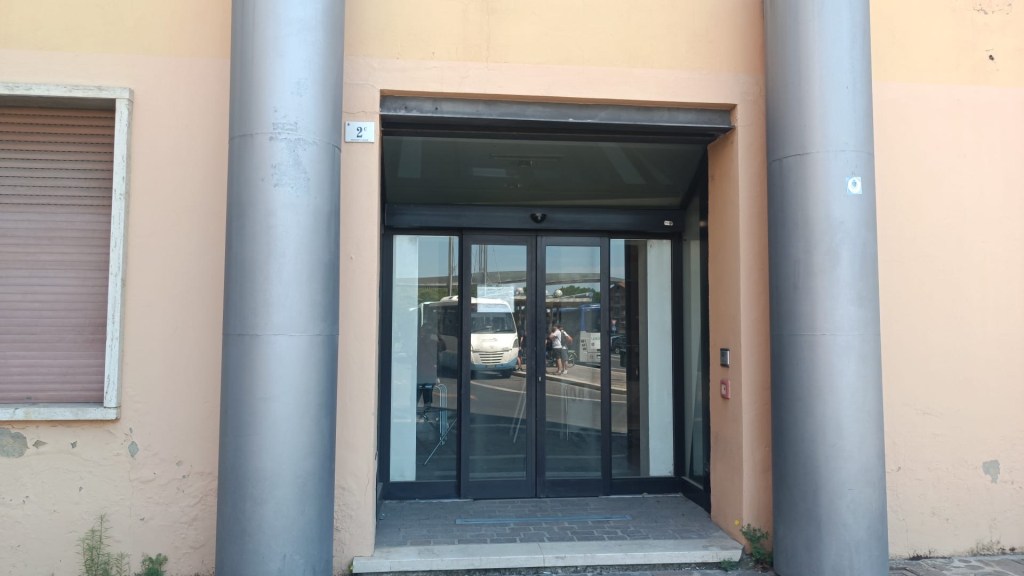 Main entrance of a building with glass sliding doors, framed by two large gray columns and a peach-colored wall.