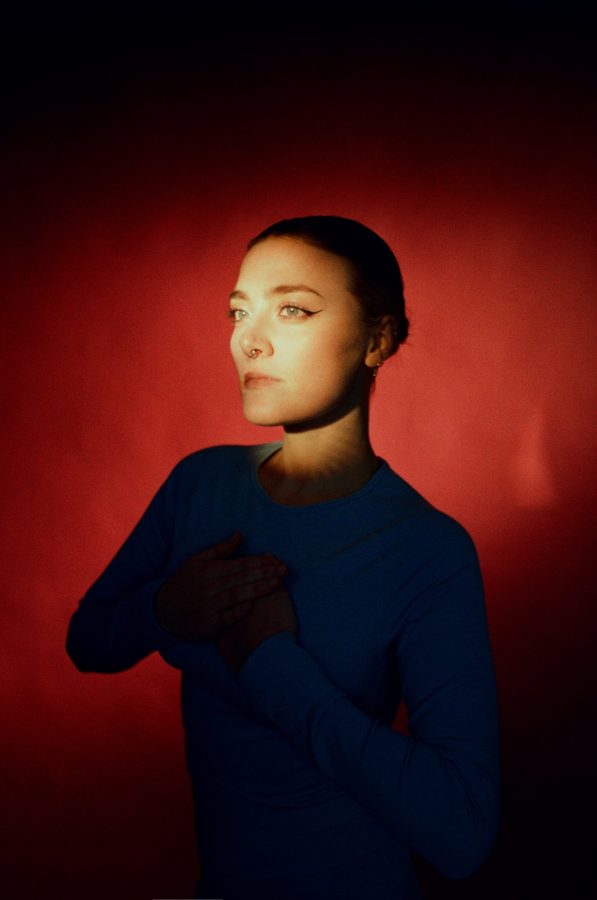 Ritratto di un'artista con luce che colpisce il volto, sullo sfondo rosso, che esprime introspezione e creatività.