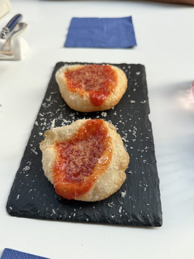 Due piccole porzioni di pane con salsa di pomodoro e formaggio grattugiato su un piatto di ardesia nera.