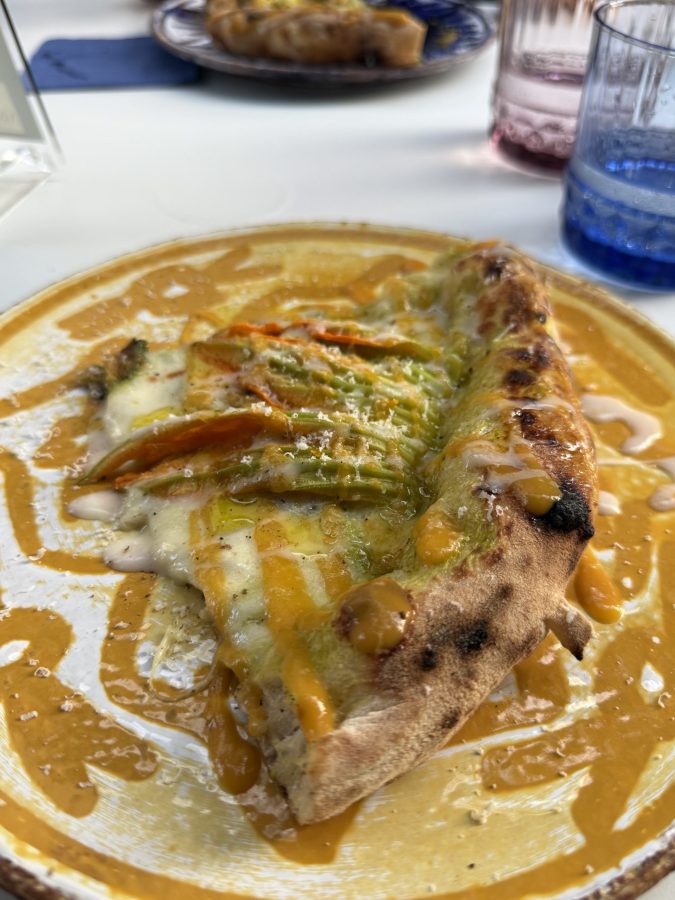 Una fetta di pizza napoletana con un cornicione ben cotto, guarnita con ingredienti freschi e una salsa cremosa su piatto bianco decorato.