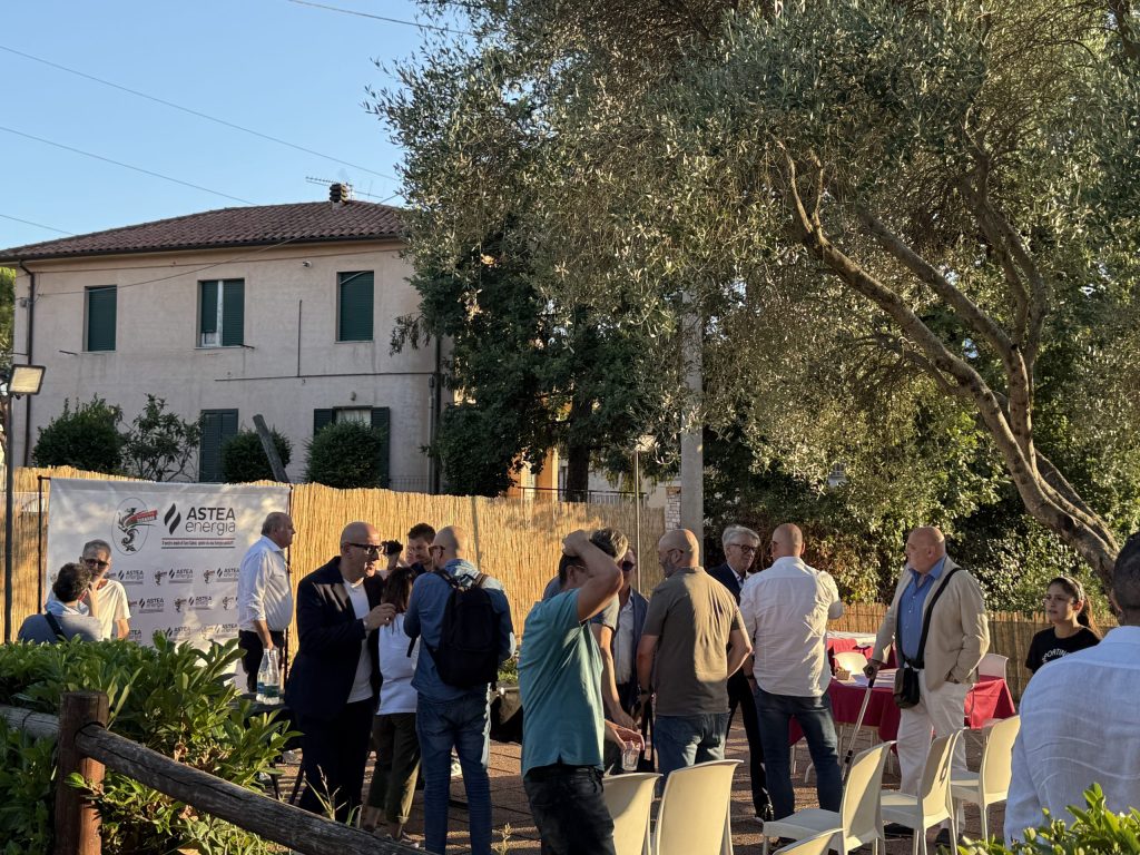 Rappresentanti e autorità discutono durante la conferenza stampa all'aperto, con tavoli apparecchiati e un'insegna di sponsor sullo sfondo.