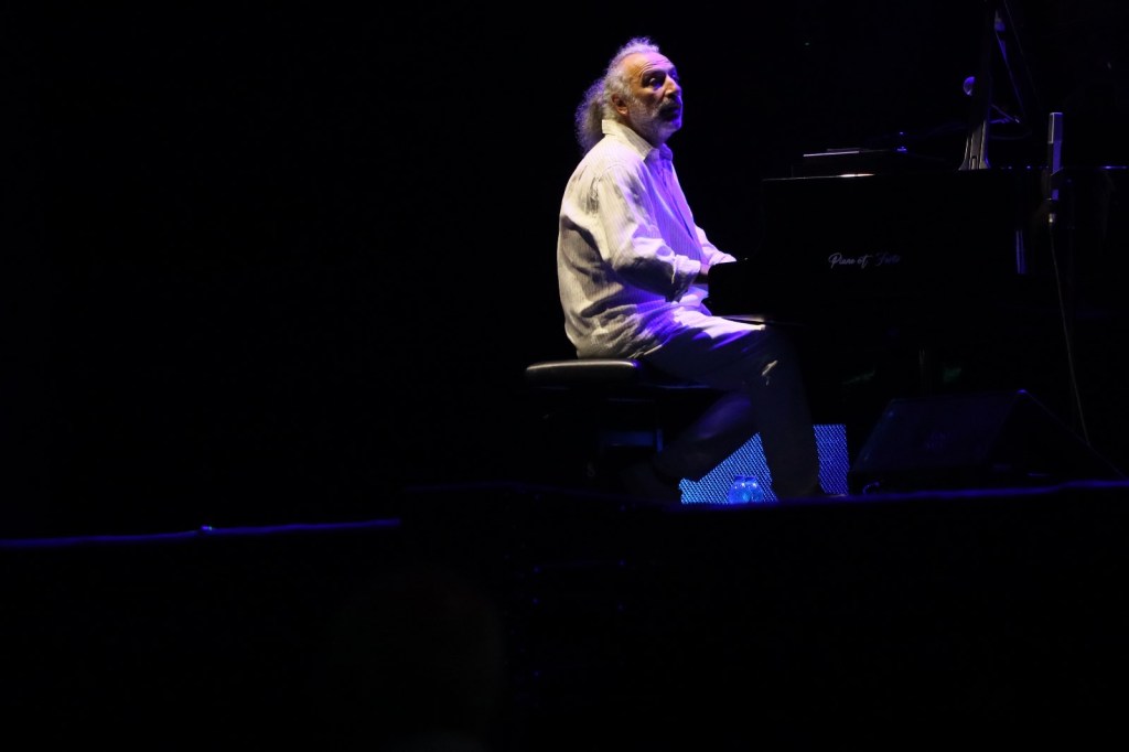 A musician playing the piano on stage under dramatic lighting.