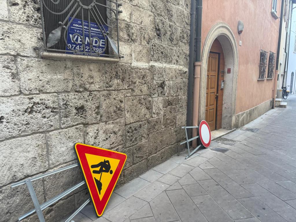 Un angolo di una strada con segnali di deviazione e lavori abbandonati, accanto a un edificio storico.