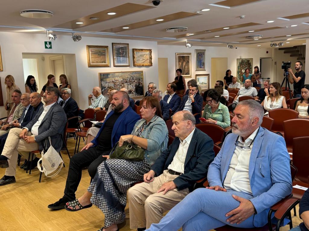 A gathering of people seated in a room with artwork on the walls, engaged in a discussion or presentation.