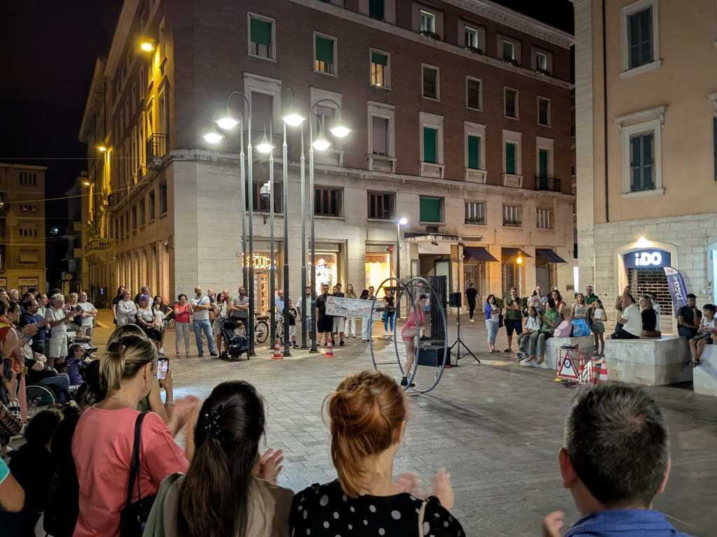 Spettacolo serale di circo in piazza della Repubblica con numeroso pubblico applaudente durante la performance.