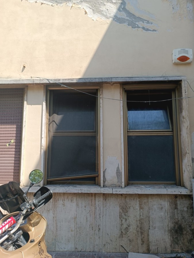 Two windows on an exterior wall, one partially open, with peeling paint and a motorbike parked in the foreground.