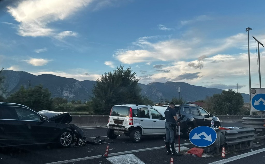 A car accident on a highway involving three vehicles, with police on the scene and mountains in the background.