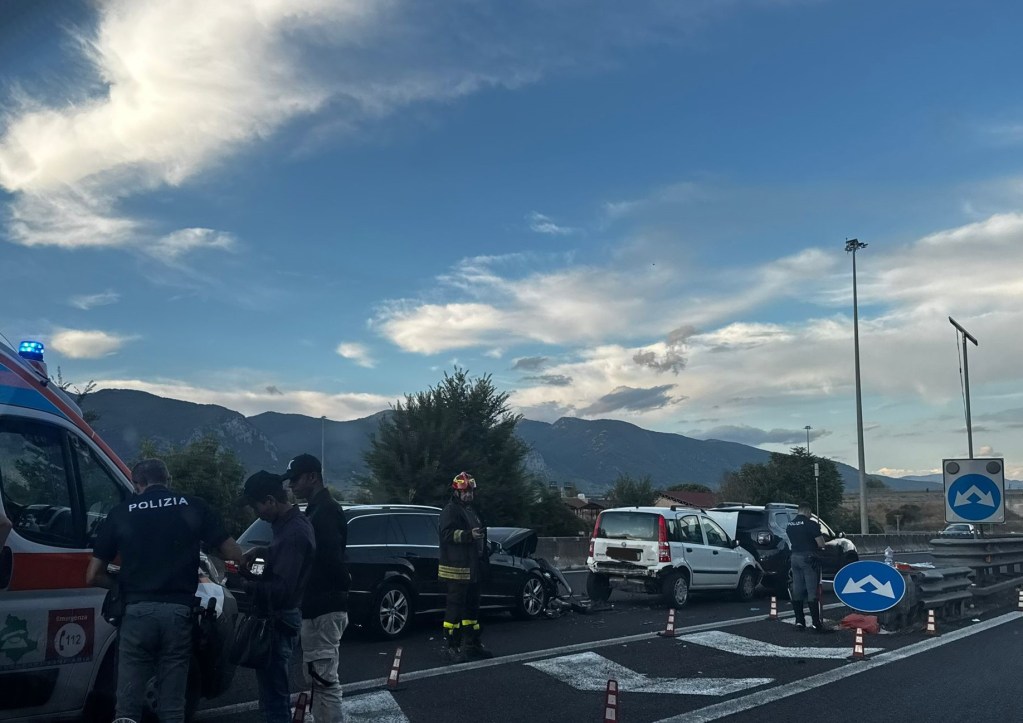Emergency responders attending to a car accident on a highway, with multiple vehicles involved and a scenic mountain backdrop.