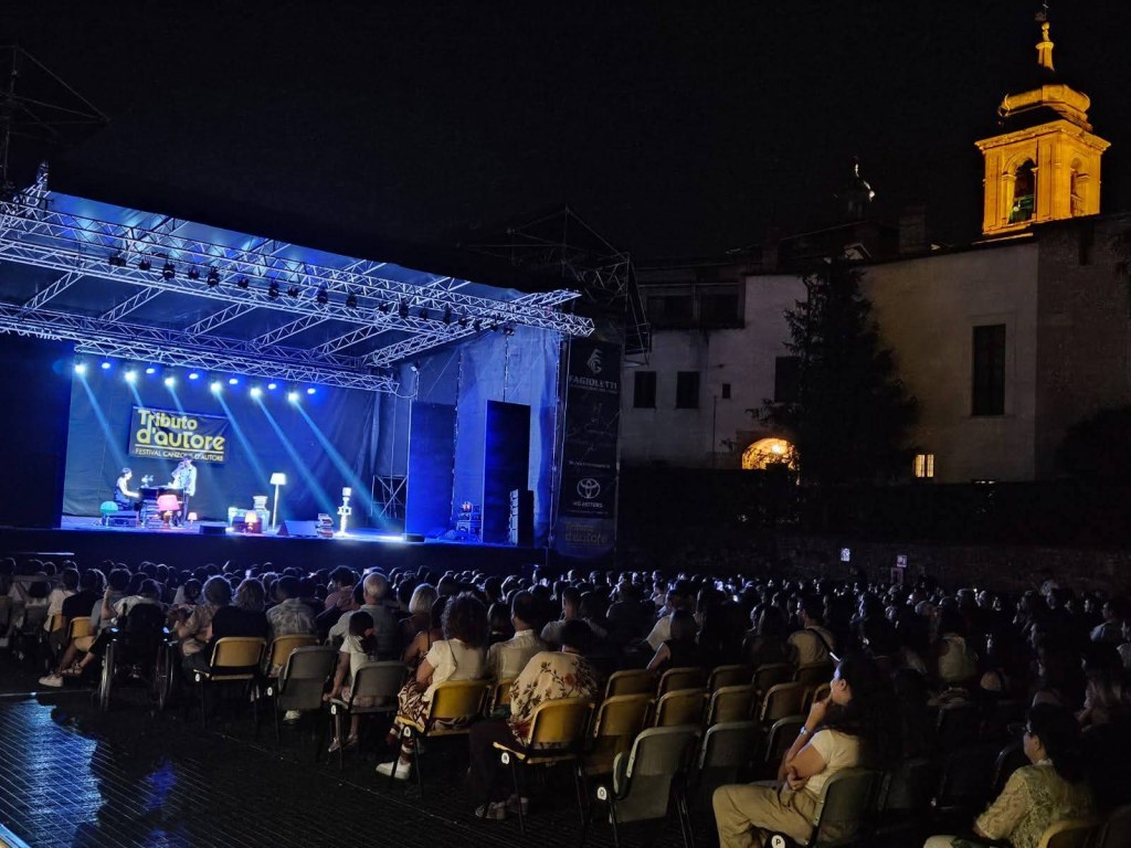 Un concerto di Michele Bravi durante il Tributo d'Autore all'Anfiteatro Romano di Terni, con il pubblico in platea e le luci sul palco.
