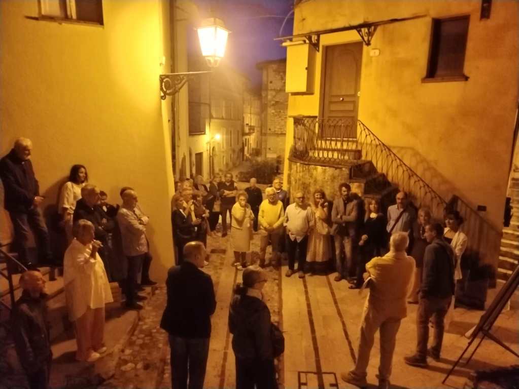Un gruppo di persone riunite in una strada illuminata da un lampione, mentre partecipano a un evento culturale nel borgo di Torreorsina.