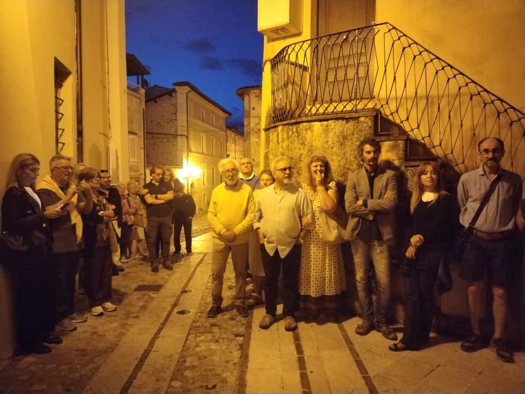 Gruppo di persone riunite in una strada del borgo di Torreorsina, con luci soffuse e atmosfera serale.