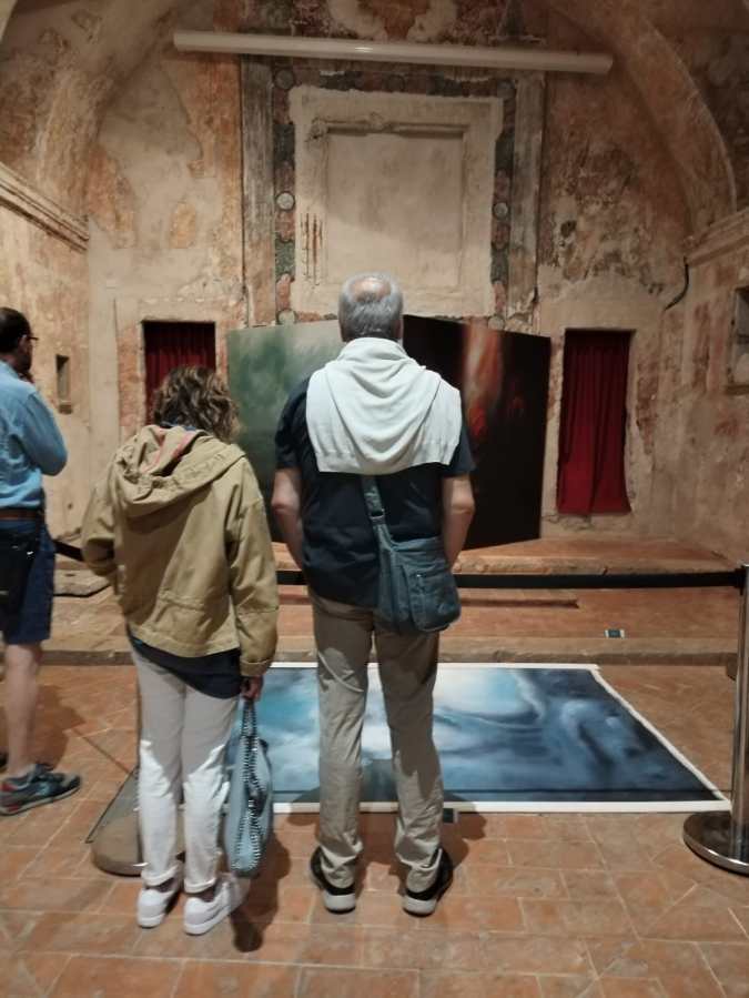 Due visitatori ammirano le opere d'arte esposte in una chiesa storica, con dipinti ben visibili sul retro.