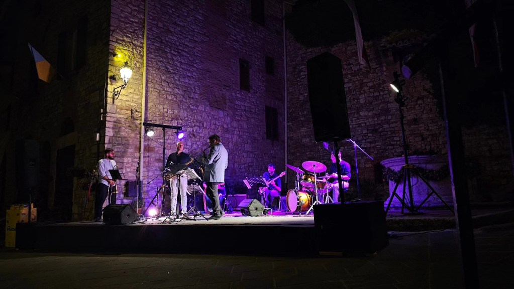 Un gruppo di musicisti si esibisce su un palco illuminato a Corciano durante l'Agosto Corcianese.