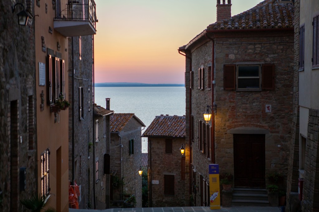 Vista di un vicolo in un borgo al tramonto, con case in pietra e luce soffusa che si riflette sul lago.