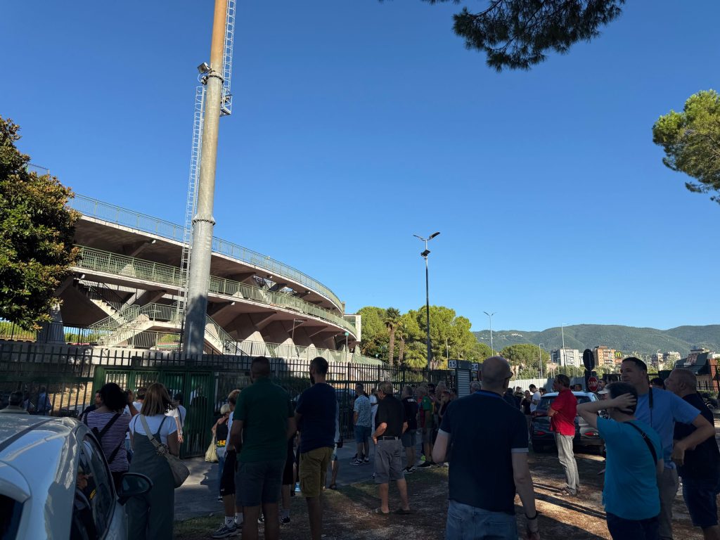 Una folla di tifosi si raduna davanti allo stadio 'Libero Liberati' per assistere agli allenamenti della Ternana, sotto un cielo sereno e blu.