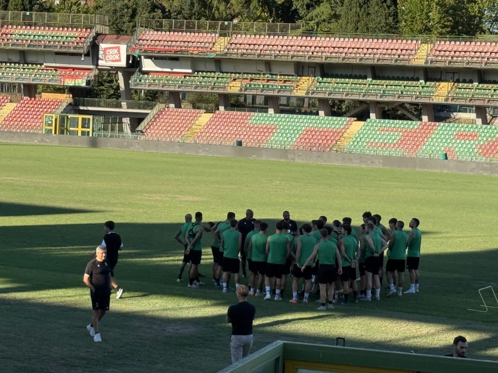Allenamento della Ternana allo stadio Libero Liberati, con giocatori riuniti in cerchio per la strategia, mentre sullo sfondo si vedono i seggiolini vuoti dello stadio.