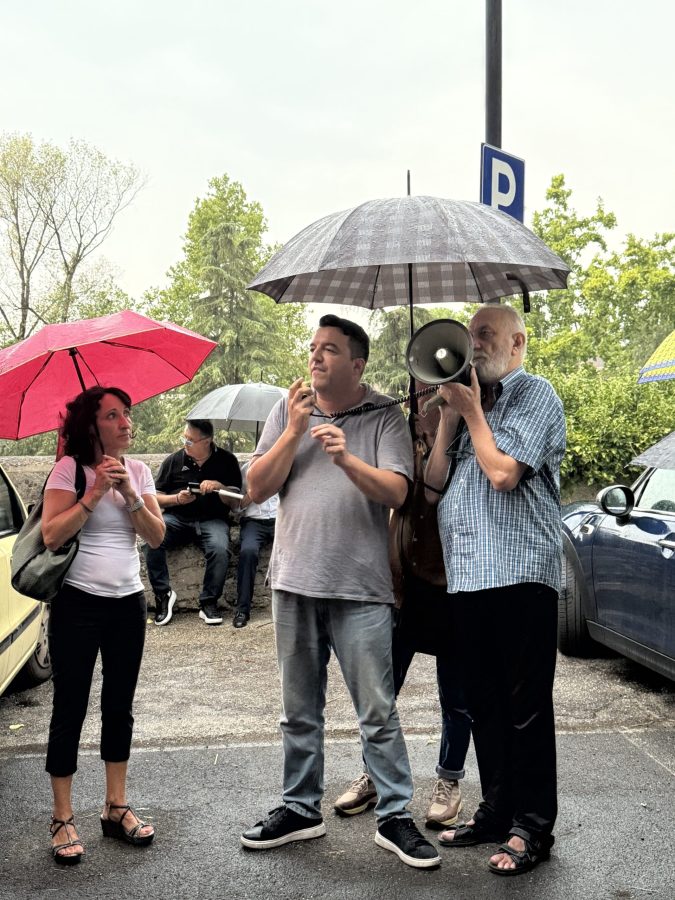 Manifestanti con ombrelli durante una protesta contro l'abbattimento di alberi, con alcune persone che ascoltano attentamente un relatore.