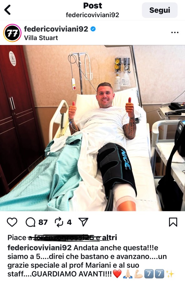 Federico Viviani in ospedale dopo un intervento al ginocchio, sorridente con un pollice in su e una fasciatura sul ginocchio sinistro, indossando una maglietta bianca e un lenzuolo azzurro.