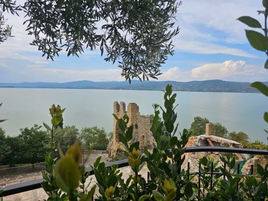 Vista panoramica sul lago Trasimeno con rovine storiche in primo piano e vegetazione circostante.