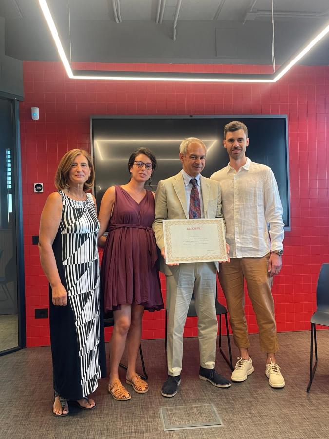 Un gruppo di quattro persone posa sorridente per una foto in un ambiente moderno, con pareti rosse, mentre uno di loro tiene un riconoscimento in mano.