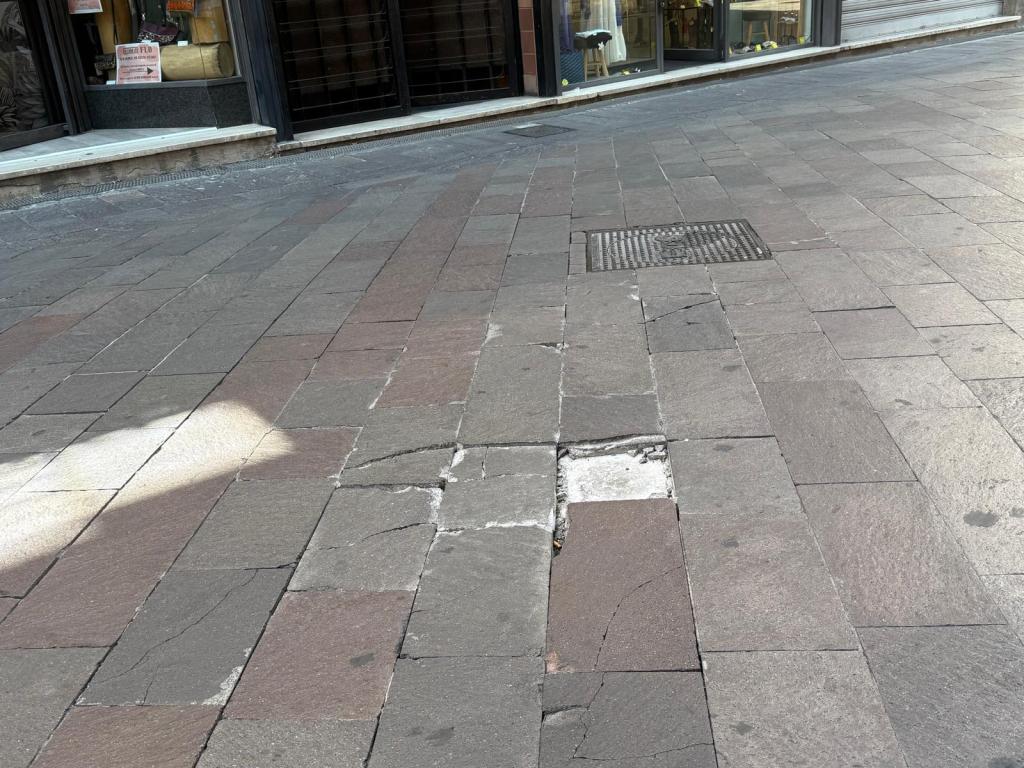 A cobblestone street with several cracked tiles and a metal grate visible.