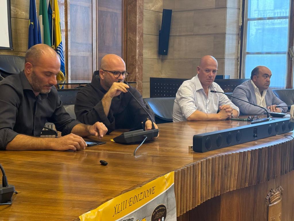 Conferenza stampa per la presentazione della 43esima edizione dell'Agosto Stronconese, con relatori seduti a un tavolo e bandiere sullo sfondo.