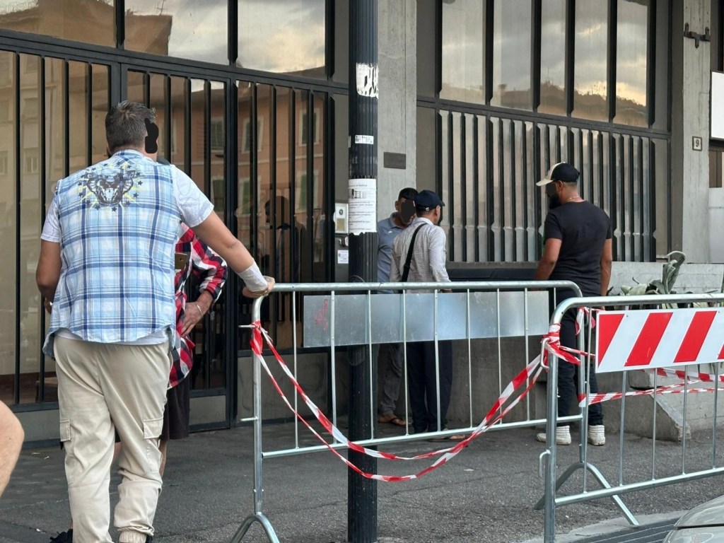 Persone che si trovano davanti a un edificio con barriere di sicurezza e transenne.