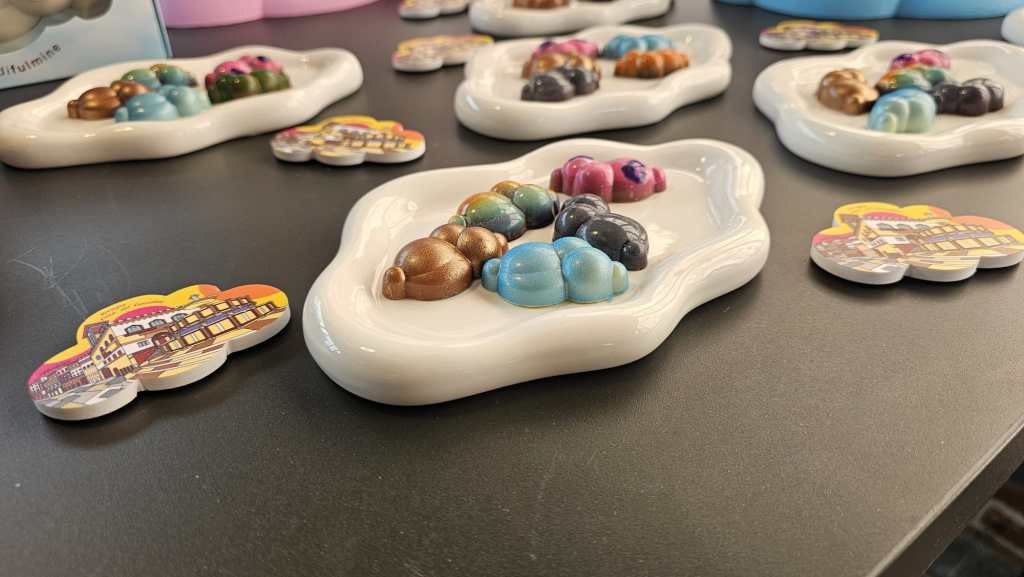 Selezione di cioccolatini colorati a forma di nuvole su piatti bianchi, con alcuni cartellini illustrati accanto.