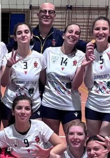 Una squadra di volley femminile in posa con il coach, sorridendo e indossando le divise della squadra.
