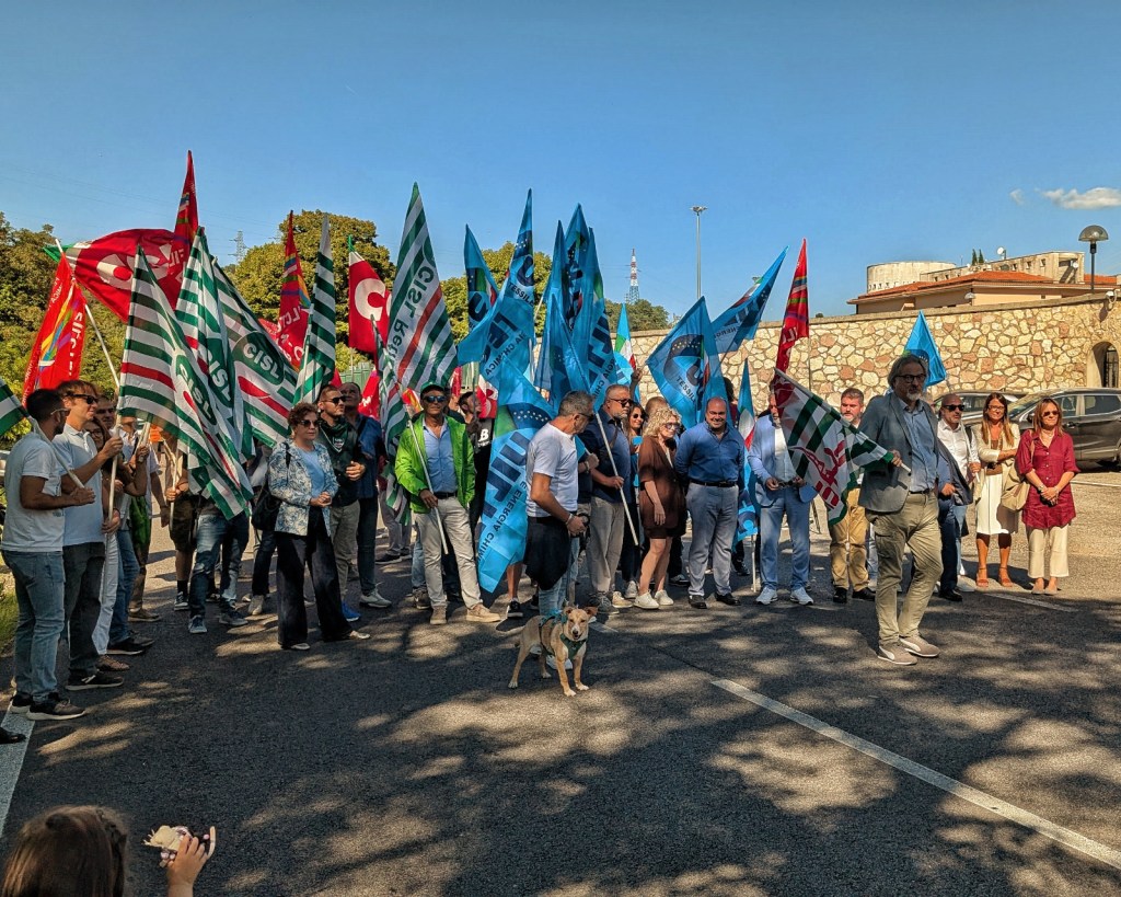 Un gruppo di manifestanti con bandiere dei sindacati si riunisce davanti a un edificio per protestare contro la chiusura del Posto di Teleconduzione di Terni.