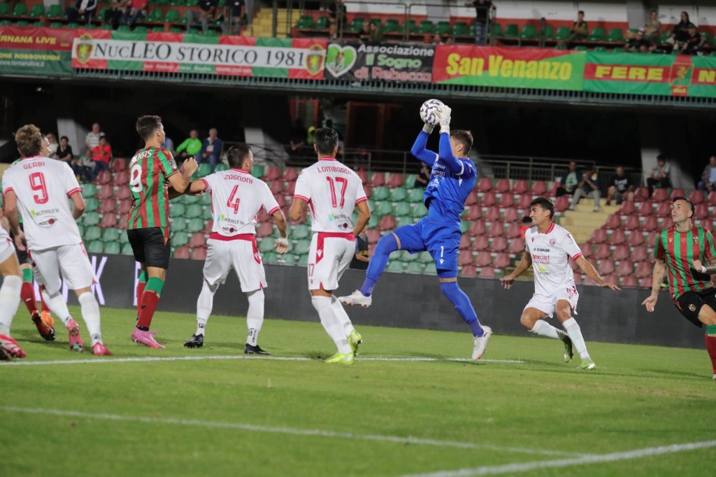 Goalkeeper making a save during a soccer match while players from both teams watch.