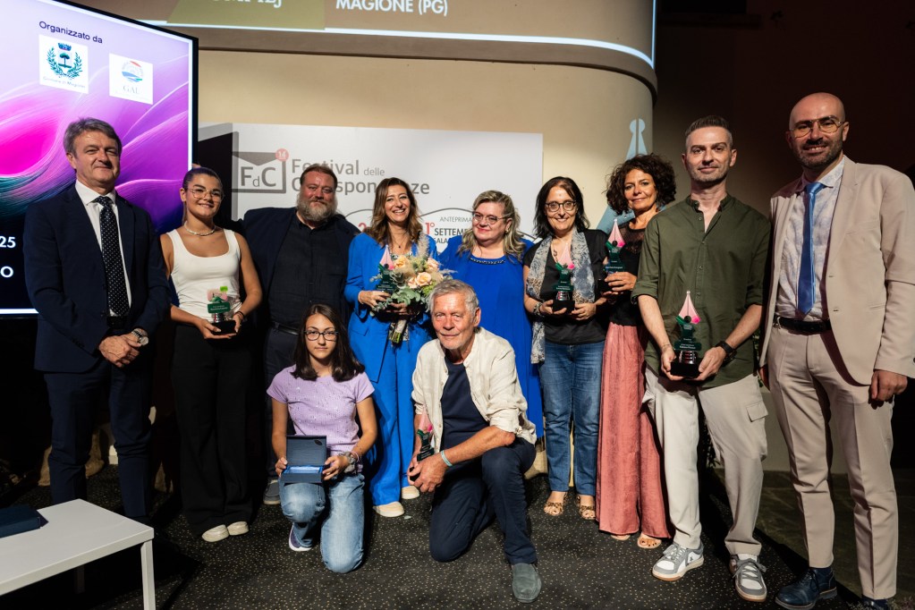 Un gruppo di premiati e organizzatori posa per una foto durante la 14esima edizione del Festival delle Corrispondenze a Magione, mostrando i trofei ricevuti.