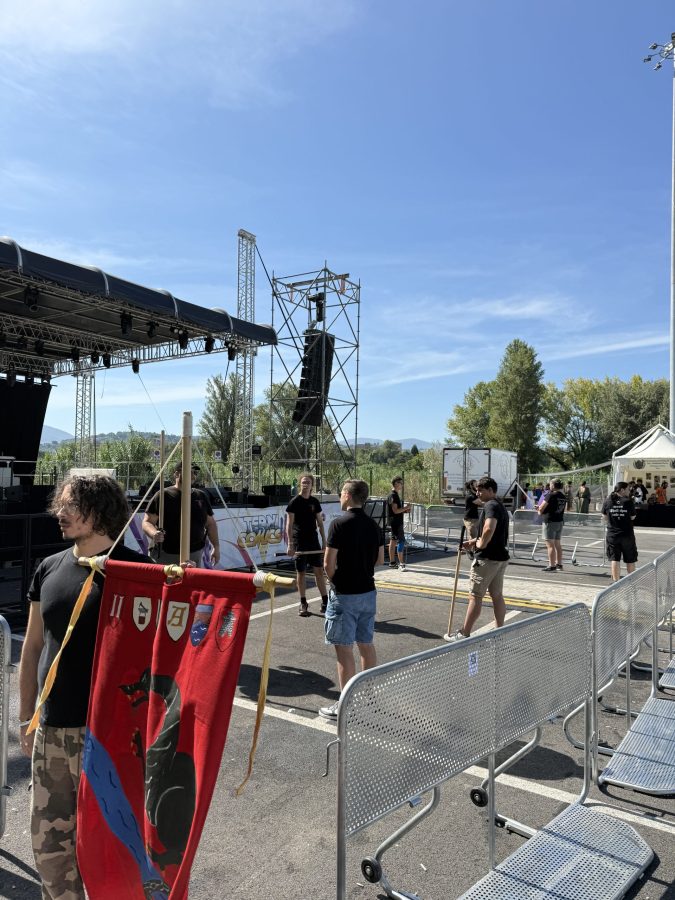 Gruppo di partecipanti al Terni Comics, con un palco allestito sullo sfondo e una bandiera rossa decorata, sotto un cielo sereno.