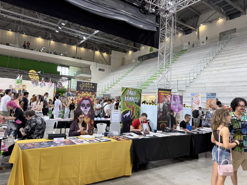 Una vista dell'evento Terni Comics all'interno del Palaterni, con diversi stand di fumetti e artisti, visitatori che interagiscono e un'atmosfera vivace.