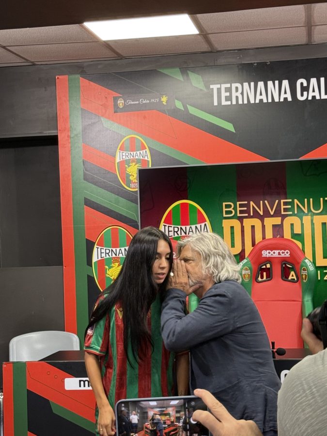 Claudia Rizzo durante la conferenza stampa di presentazione come presidente della Ternana, in abbigliamento sportivo, mentre discute con Massimo Ferrero sullo sfondo di una grafica della squadra.