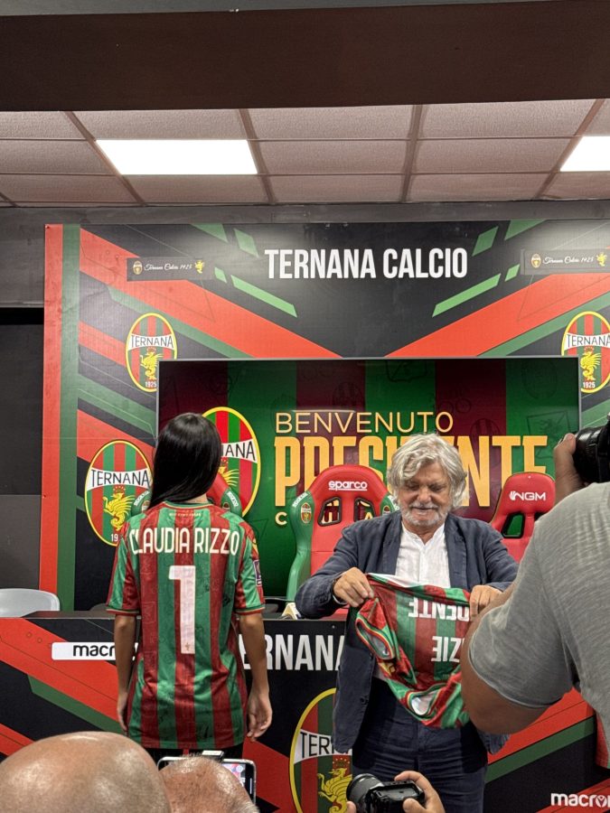 Claudia Rizzo is welcomed as the new president of Ternana Calcio, holding her jersey while standing next to Massimo Ferrero in a press conference setting.
