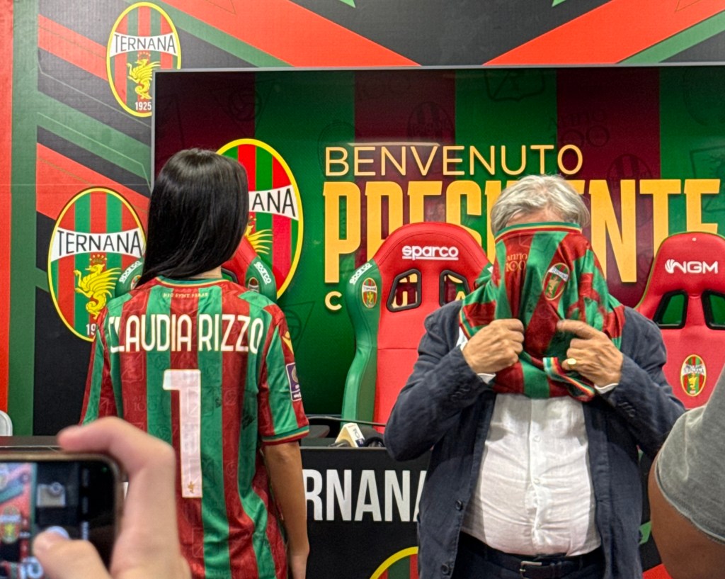 Claudia Rizzo indossa la maglia della Ternana, mentre Massimo Ferrero si copre il viso con un'altra maglia durante una conferenza stampa.