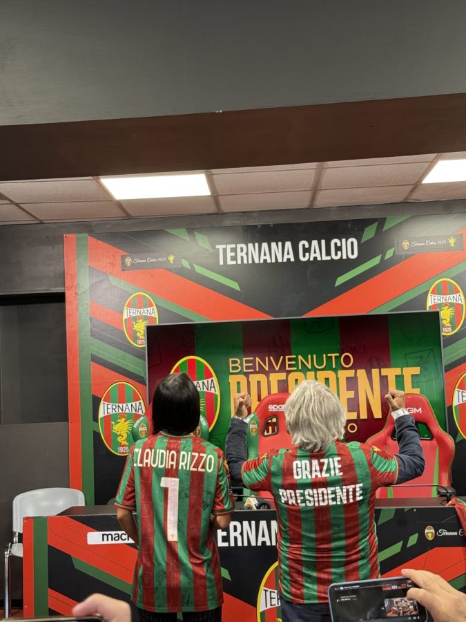 Due donne in maglietta con i colori della squadra Ternana, una con 'CLAUDIA RIZZO' e l'altra con 'GRAZIE PRESIDENTE'. Sono di spalle, davanti a una scrivania con la scritta 'BENVENUTO PRESIDENTE'.
