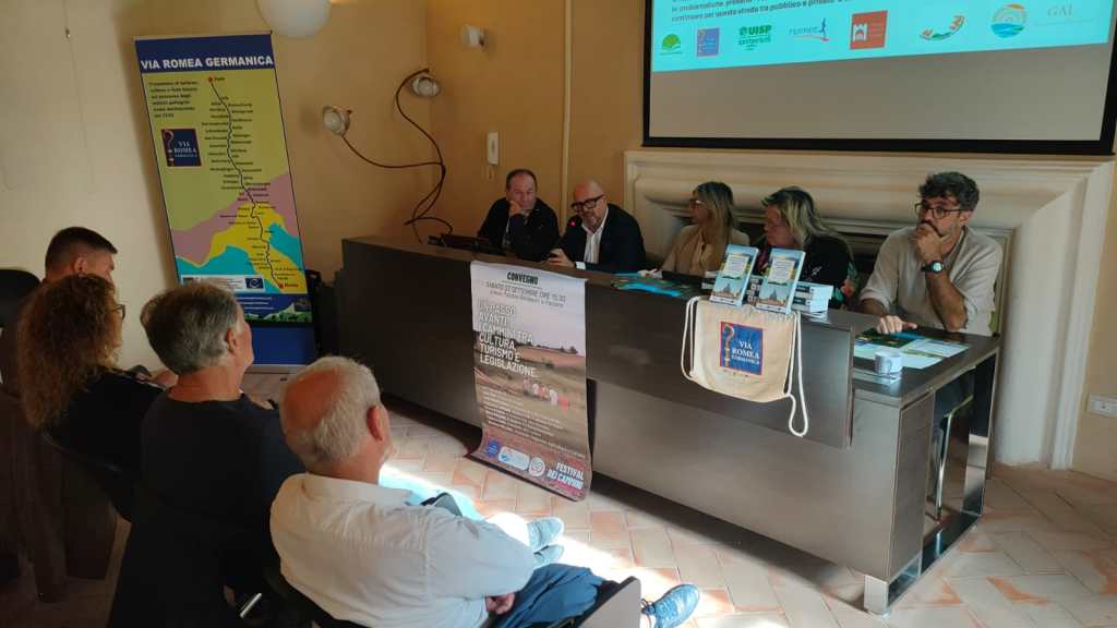 Conference on the promotion of the Via Romea Germanica, featuring speakers at a table with a map and promotional materials.
