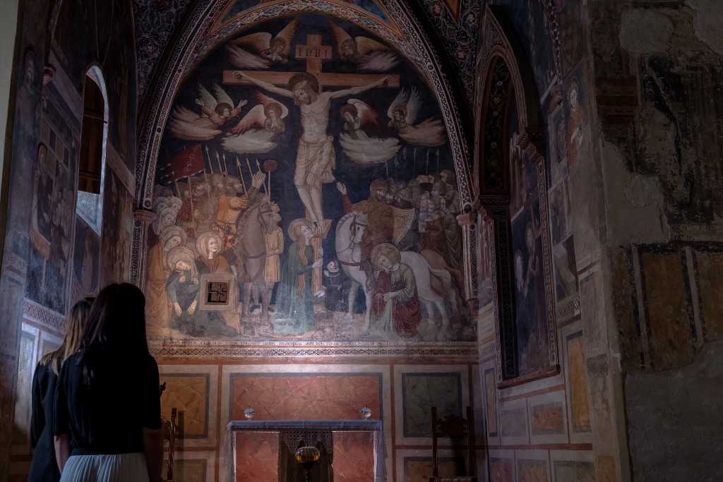 Due visitatori osservano un affresco che rappresenta la crocifissione, all'interno di una chiesa a Montefalco.