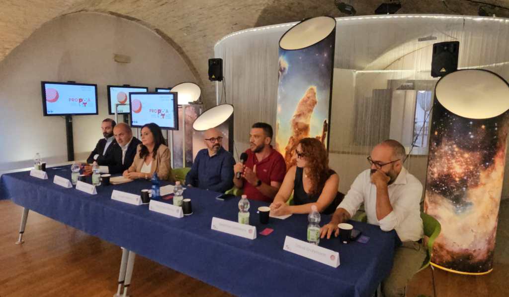 Evento di presentazione dell'offerta formativa del Post - Museo della scienza di Perugia, con relatori seduti a un tavolo e display interattivi sullo sfondo.