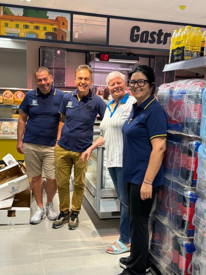 Quattro persone sorridenti che posano all'interno di un negozio, con prodotti in esposizione davanti a loro.