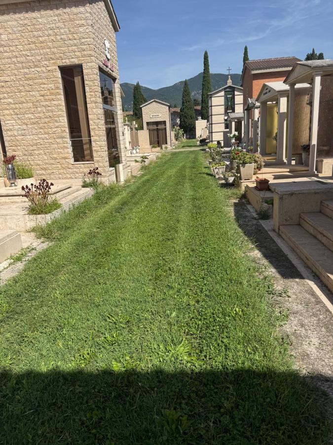 A pathway lined with well-maintained grass, leading through a cemetery with mausoleums and tombs on either side, set against a backdrop of mountains and blue sky.