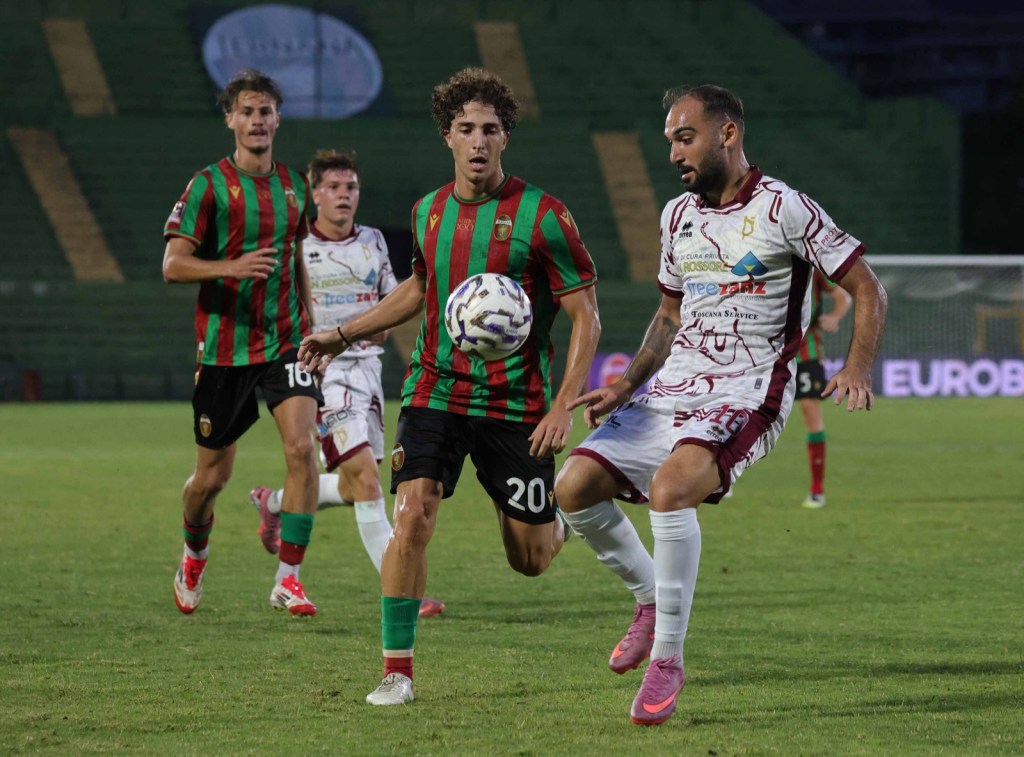Giocatori di calcio in azione durante una partita, con due squadre in maglie a strisce colorate, uno dei giocatori sta cercando di conquistare il pallone.