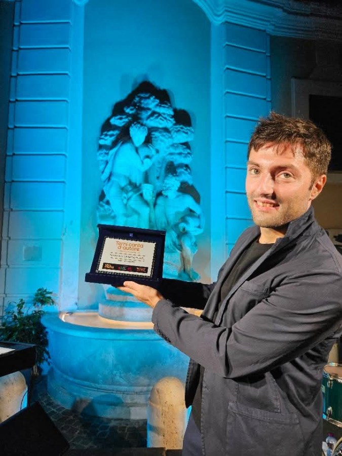 A man holding an award in front of a blue-lit statue in a decorative setting.