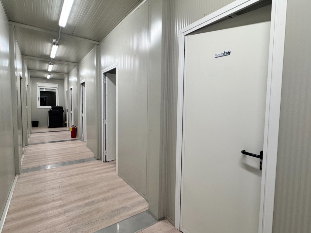 Interno di un campo base con corridoio e porte chiuse, illuminato da luci a LED.