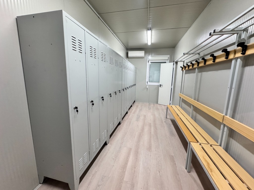 Interno di un spogliatoio con armadietti metallici grigi e panche di legno.