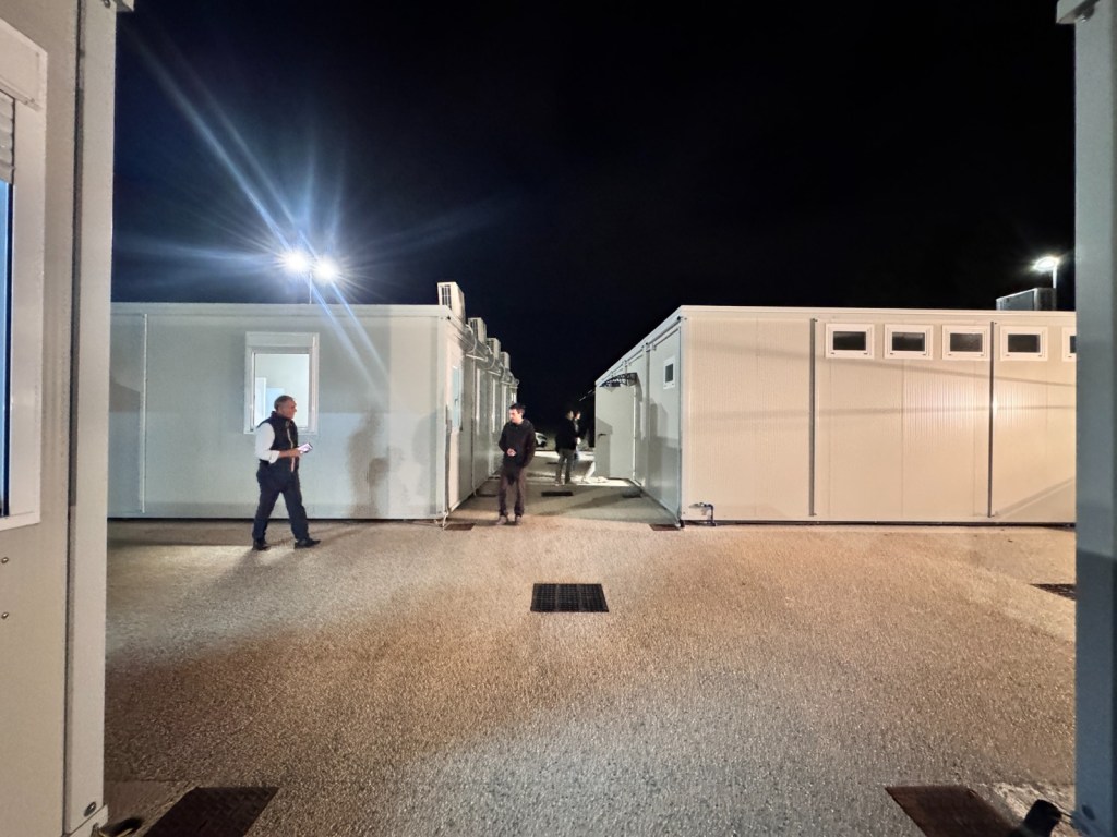 Immagine notturna del nuovo campo base di Vestricciano, con moduli prefabbricati e persone che camminano nell'area.